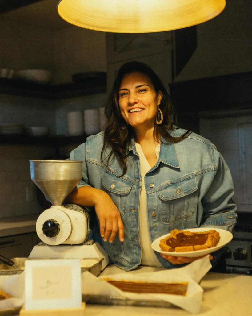 The Barz Lady in her kitchen with her grain mill and a plate of barz